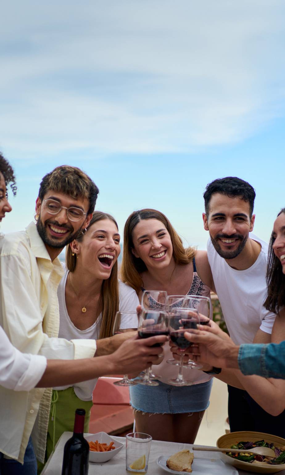 Vertical. Gathering smiling young friends toasting glasses wine standing celebrating a event on terrace. Diverse people drinking alcoholic beverages at lunch enjoying weekend and leisure time outdoor