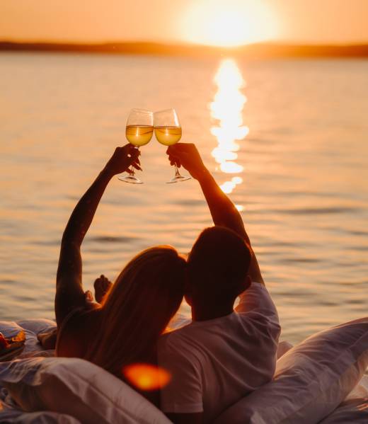 Silhouettes of a happy couple raising glasses on a summer evening near the sea at sunset.