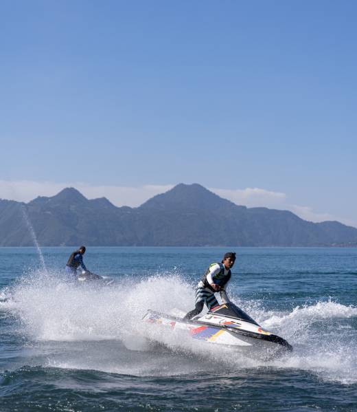 Two young Hispanic men navigate jet-skis on the waters of Atitlan Lake, Guatemala, engaging in recreational water activity against the scenic backdrop of the lake's natural beauty